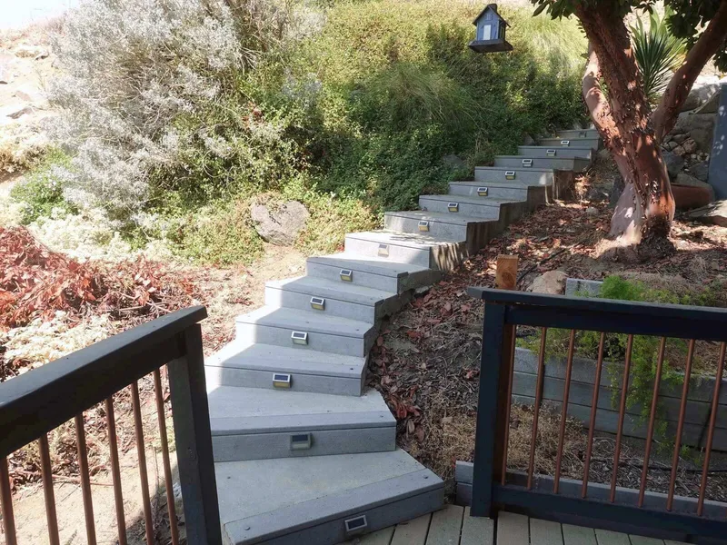 Concrete garden steps with small path lights climbing the hillside beside a wooden railing